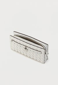 Λευκό πορτοφόλι με υφή, με φερμουάρ και μπροστινή τσέπη, με ασημί στρογγυλό λογότυπο στη αγκράφα, απομονωμένο σε ανοιχτό φόντο.