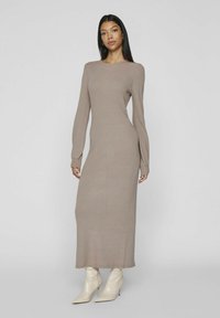 Abito lungo a maniche lunghe beige lavorato a maglia, con scollatura rotonda e silhouette dritta, abbinato a stivali alla caviglia crema. Tessuto liscio e design semplice.
