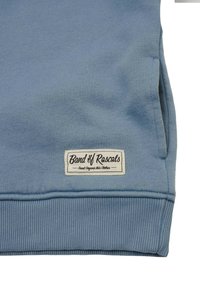 Vaaleansininen collegepaita, joka on valmistettu pehmeästä puuvillasta. Paidan hihoissa ja helmassa on joustavat resorit, ja etuosassa on ommeltu etiketti, jossa lukee "Band of Rascals".