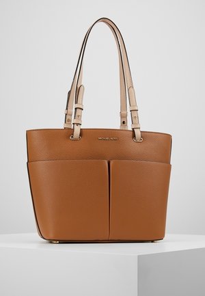 Bruine leren tote bag met dubbele voorvakken, twee beige handvatten en een gouden logo. Heeft een gestructureerd ontwerp en een getextureerde afwerking.