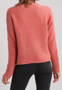 Pull en maille rose avec un motif texturé, épaules tombantes et manches longues. Coupe décontractée, longueur raccourcie à la taille.