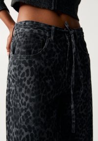 Pantalones de mezclilla negros con un patrón de leopardo, con cintura ajustable, bolsillos laterales y un corte relajado.