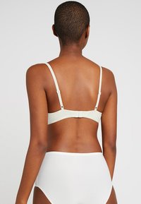 Light green bra with adjustable straps and back clasp. Made of smooth fabric with minimal detailing, paired with plain white high-waisted underwear.