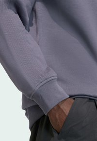 Jasnofioletowa bluza z prążkowanymi mankietami i detalicznym przeszyciem na rękawach. Gładka faktura, zestawiona z ciemnoszarymi spodniami.