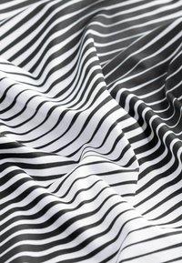 Svart och vitrandig textil med mjuk struktur. Ränderna är vågiga och varierar i bredd, vilket skapar en dynamisk visuell effekt.