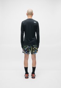 Svart langermet treningsskjorte, mønstrede svarte shorts med fargerike blomsterdesign, svarte sokker og røde treningssko.