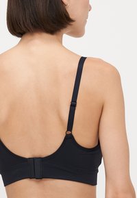 Melnas krūšturis ar regulējamām siksnām, gludu apdari un aizmugurē esošu āķa un acs aizdari, kas izstrādāts, lai nodrošinātu komfortu un atbalstu.