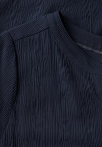 Sininen paita, jossa on tekstuuroitu, aaltoileva kangas. Siinä on pyöreä kaula-aukko ja lyhyet hihat, sekä sileä helma ja rento muotoilu.