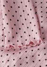 Różowy materiał o fakturze z wypukłymi czarnymi kropkami i falistymi liniami, z falbanką na krawędzi.