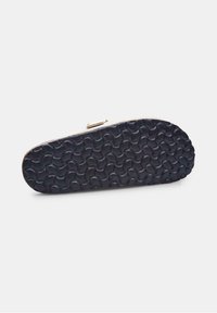 Footwear sole featuring a textured black rubber material with a wavy pattern. The edge is light-colored, smooth, and rounded.