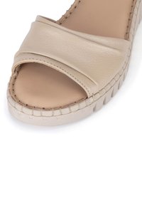 Sandalia beige de punta abierta con suela cosida y amplia correa frontal de cuero, que presenta una plataforma ligeramente elevada con suela exterior texturizada antideslizante.