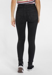 I jeans skinny neri in denim presentano un alto girovita, due tasche posteriori e una leggera sbiaditura. Abbinati a scarpe nere e a una maglietta a righe.