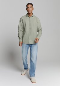 Lichtgroene blouse met lange mouwen van zachte stof, met een button-down voorkant en een relaxte pasvorm, gecombineerd met lichtblauwe jeans en sneakers.