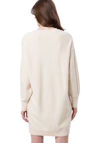 Cremefarbenes, oversize Strickkleid mit langen Ärmeln, gerippten Bündchen und rundem Halsausschnitt. Weicher, strukturierter Stoff mit lockerer Passform.