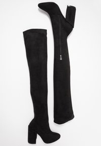 Botas negras hasta la rodilla de ante, con un tacón cuadrado y una cremallera lateral para facilitar su uso. Textura suave con una forma ajustada.