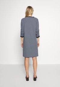 Robe à carreaux bleus et blancs avec manches longues, coupe au genou, et accents noirs aux poignets, dotée d'un col rond simple.