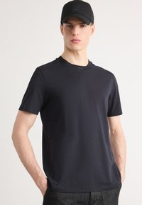 Σκούρο ναυτικό μπλουζάκι κοντομάνικο φτιαγμένο από λεία ύλη, με ριγωτό λαιμόκοψη και διακριτική λεπτομέρεια λογότυπου κοντά στον γιακά.