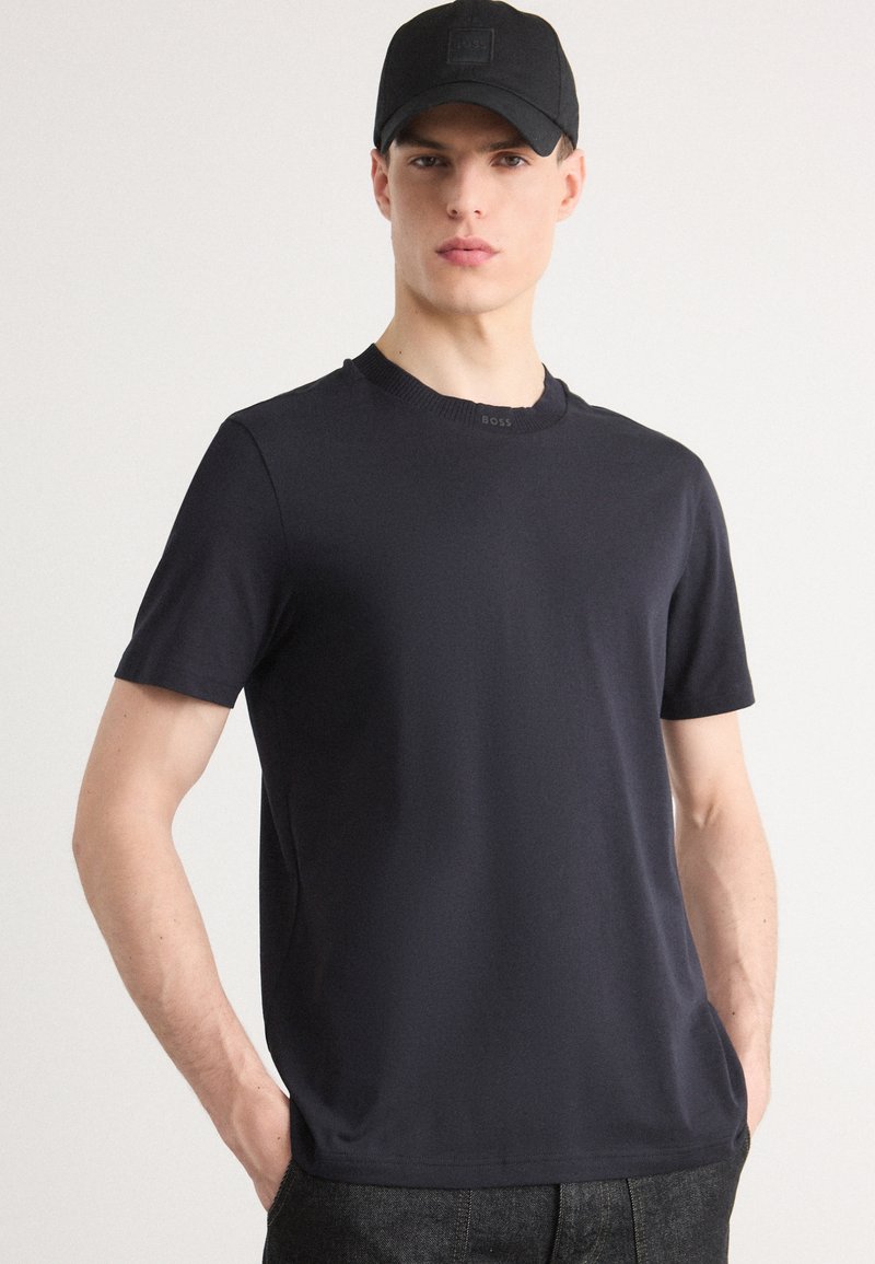 Σκούρο ναυτικό μπλουζάκι κοντομάνικο φτιαγμένο από λεία ύλη, με ριγωτό λαιμόκοψη και διακριτική λεπτομέρεια λογότυπου κοντά στον γιακά.