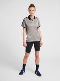 Lichtgrijze polo met een zwarte kraag en schouderstrepen, gecombineerd met zwarte fietsbroek en marineblauwe sportschoenen.