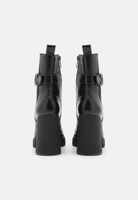 Schwarze Leder-Ankelboots mit glatter Oberfläche, hohen Blockabsätzen, seitlichen Reißverschlüssen und dekorativen silbernen Schnallenakzenten.