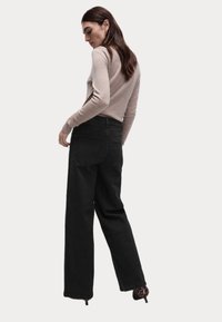 Černé široké džíny vyrobené z textilního materiálu, v kombinaci s přiléhavým béžovým topem s dlouhým rukávem. Modelka je zobrazena zezadu, což zdůrazňuje siluetu outfitu.