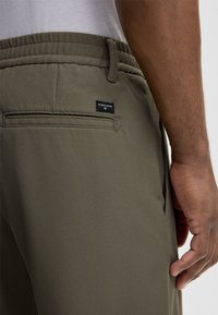 Olijfgroene broek van een textuurstof, met een elastische tailleband, zijzakken en een achterzak met een label.
