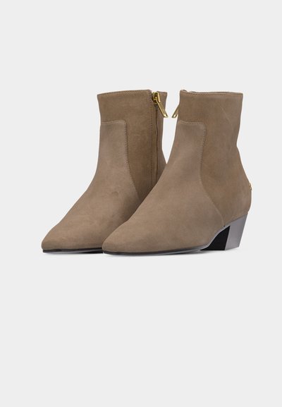 Ζευγάρι μποτάκια αστραγάλου από σουέντ σε χρώμα τόουπ με μυτερές μύτες, χρυσά πλαϊνά φερμουάρ και χαμηλά κεκλιμένα τακούνια σε απλό λευκό φόντο.