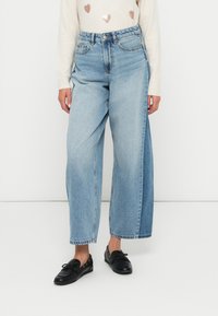 Helle blaue weite Jeans aus Denim mit einer verblassten Textur, featuring eine hohe Taille und ein klassisches Fünf-Taschen-Design. Darunter schwarze Schuhe.
