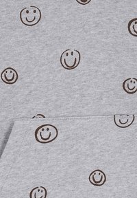 Grau Stoff mit einer weichen Textur, versehen mit einem wiederholten Muster von braunen Smiley-Gesichtern. Einfaches Design mit einer lässigen, verspielten Ästhetik.