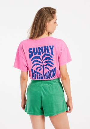Roze oversized t-shirt met blauwe tekst "SUNNY AFTERNOON" voorzien van grafisch ontwerp. Gecombineerd met groene shorts van zachte, gestructureerde stof.