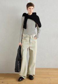 Ριγέ μπλούζα με μακριά μανίκια, μαύρος πλέκτης στους ώμους, φαρδιά τζιν παντελόνια σε ανοιχτό μπλε χρώμα και μαύρα παπούτσια; κρατώντας μια μαύρη τσάντα.