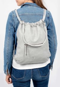 Sac à dos en nylon perforé gris avec un haut resserré et des bretelles ajustables. Présente une poche zippée à l'avant et des accents à texture lisse.
