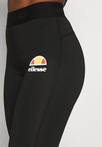 Czarne legginsy z wysokim stanem, wykonane z elastycznego materiału. Logo ma kolorowy łuk i białe napisy.