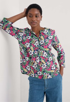 Blusa floreale con sfondo blu navy, caratterizzata da fiori e foglie multicolori, scollo rotondo e maniche a tre quarti. Abbinata a jeans blu.