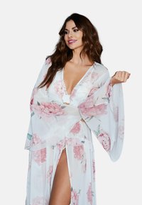 Przezroczysty biały kimono z różowym kwiatowym wzorem, z szerokimi rękawami, głębokim dekoltem w szpic i rozcięciem sięgającym do ud, z teksturowanej tkaniny oraz ozdobnymi guzikami.