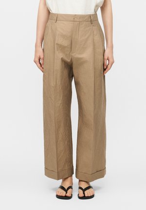 Μπεζ παντελόνι με φαρδιά μπατζάκια και ρεβέρ, φορεμένο με μαύρα σανδάλια-σαγιονάρες και λευκό τοπ, εμφανιζόμενο από τη μέση μέχρι τα πόδια.