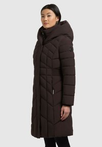 Cămașă puf închisă la culoare cu glugă, având un model țesut în formă de zigzag, deschidere cu fermoar în față și accente elastice pe laterale.