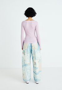 Lila lange mouw top met kantafwerking en lichtblauwe patchwork wijde broek met bloempatroon en geometrische patronen.