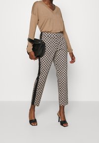 Beige top met lange mouwen gecombineerd met zwart-witte broek met een geometrisch patroon, zwarte zijpanelen en zwarte open-toe hakken.