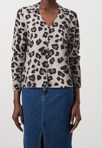 Blouse en imprimé léopard beige et noir, avec un col en V, des boutons sur le devant et des manches longues. Portée avec une jupe en denim.