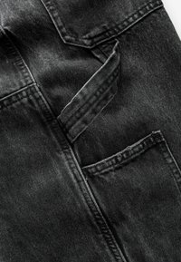 Gros plan sur un tissu en denim noir avec des coutures visibles, deux poches inclinées et une boucle de ceinture au centre.