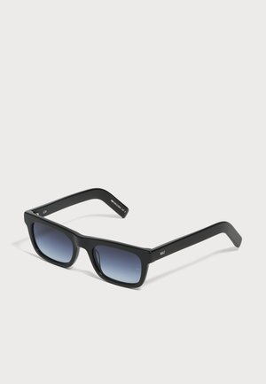 Lunettes de soleil rectangulaires noires avec verres dégradés bleu foncé et montures épaisses, posées sur une surface gris clair.