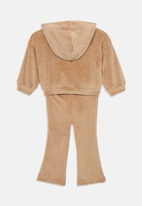 Dvojdielny outfit z jemného béžového velúru. Obsahuje kapucňový crop top s širokými rukávmi a rozšírené nohavice, ktoré sú hladké a textúrované.