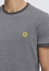 Grå bomulds t-shirt med rund hals. Har mørkegrå kant og et gult broderet kraftsymbol på brystet. Korte ærmer.