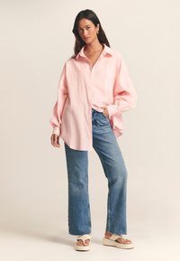 Pink and white striped oversized shirt with a pointed collar and front pocket, paired with light blue wide-leg jeans and platform sandals.