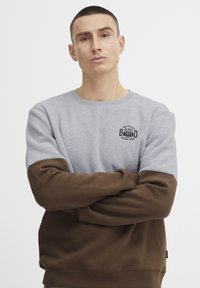 Gray and brown color-blocked sweatshirt with round neck, featuring a logo patch on the chest and ribbed cuffs and hem.