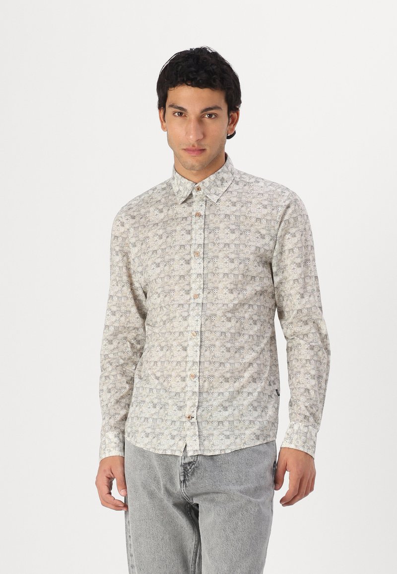 Lichtgekleurde langemouwen shirt met een geometrisch patroon, een button-down kraag en houten knopen. Draagt met lichtgrijze broek.