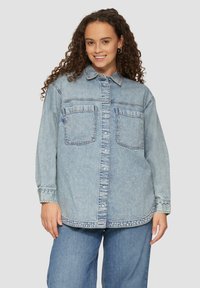 Lichtblauwe denim overhemden met lange mouwen, knoopsluiting aan de voorkant, twee borstzakken en gestikte details langs de zoom en manchetten.