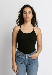 Zwarte geribbelde tanktop met dunne banden, gecombineerd met lichtblauwe spijkerbroek met hoge taille. Eenvoudig ontwerp, aansluitende silhouette.