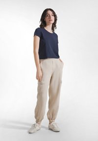 Laivastonsininen lyhythihainen t-paita, jonka kanssa on beigenväriset cargohousut sivutaskuilla ja joustavilla resoreilla lahkeissa, yhdistetty vaaleisiin lenkkareihin.